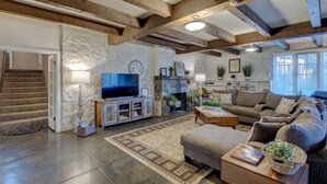 Ein geräumiges Wohnzimmer mit freiliegenden Holzbalken, einem Steinkamin, einem Fernseher und einer gemütlichen Sitzecke.
