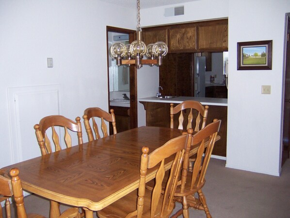 Comedor con mesa y sillas de madera, cocina con armarios de madera y una lámpara colgante.