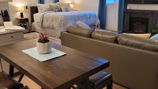 A modern living room with a sofa, a dining table with chairs, a ceiling fan, and a fireplace. - Eastwood Escape Cottage Hot Tub (Oakhurst)