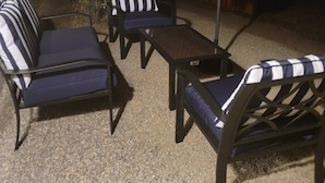 An outdoor seating area with striped cushions and a table, surrounded by a wooden fence and a small plant. - Eastwood Escape Cottage Hot Tub (Oakhurst)