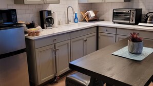 A modern kitchen with white cabinets, a stainless steel refrigerator, a microwave, a toaster, and a wooden dining table with a bench. - Eastwood Escape Cottage Hot Tub (Oakhurst)