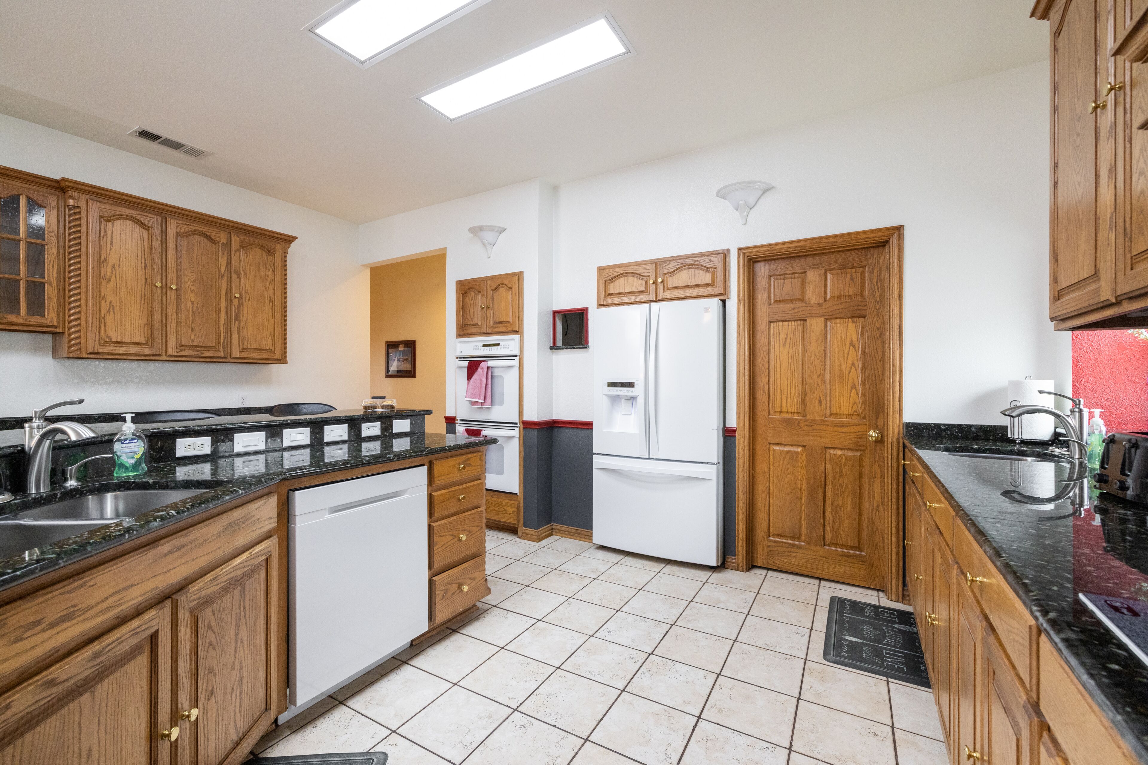 A kitchen with wooden cabinets, a white dishwasher, a stainless steel refrigerator, and a black countertop.