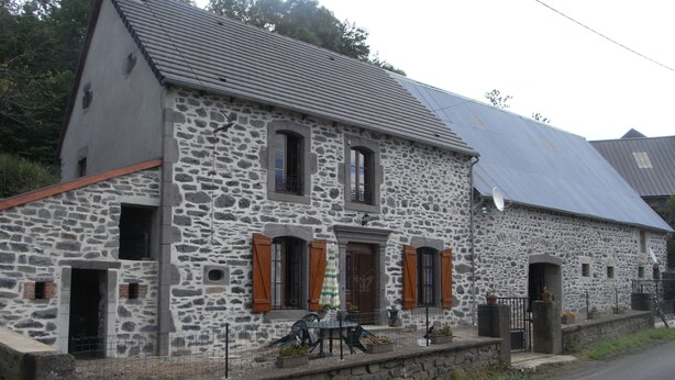 Un bâtiment en pierre doté d’un toit en pente, de nombreuses fenêtres avec volets et d’un petit porche.