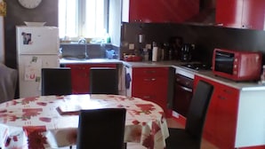 Une cuisine avec des placards rouges, un four à micro-ondes et un réfrigérateur. On y trouve une table à manger avec des chaises et une horloge au mur.