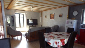 Un salon confortable avec un canapé, un téléviseur et une table à manger entourée de chaises. Il y a également un coin cuisine avec un réfrigérateur et une horloge au mur.