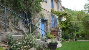Un bâtiment en pierre avec des volets bleus, un escalier et un jardin fleuri.