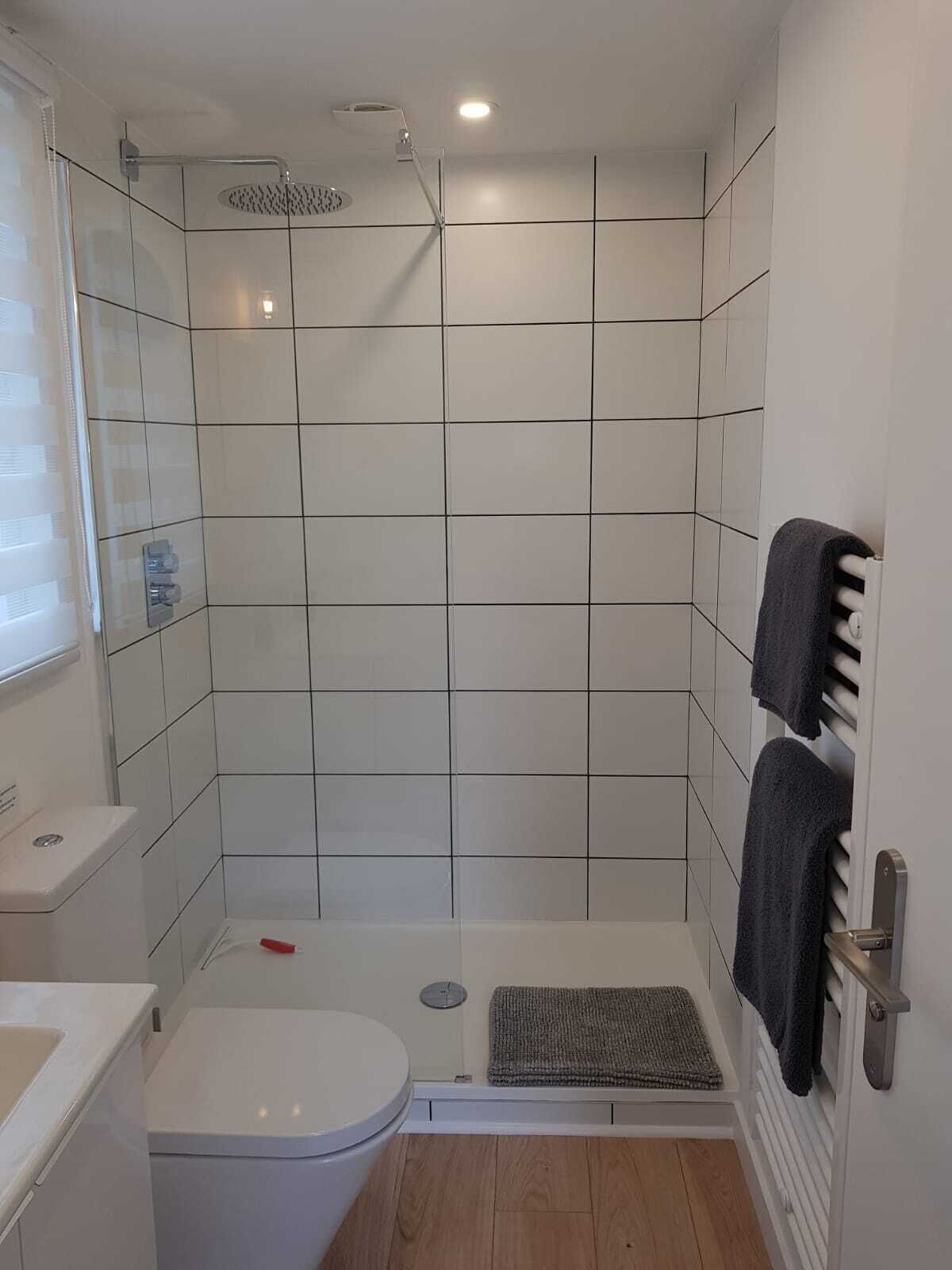 Une petite salle de bain moderne, avec des carreaux blancs, une douche, des toilettes et un porte-serviettes.