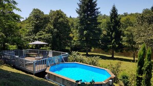 A backyard with a swimming pool, a deck with a table and chairs, and a covered seating area.