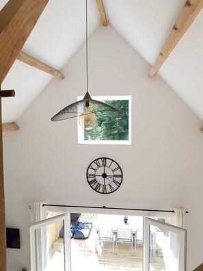 A room with a sloped ceiling, a hanging pendant light, a wall clock, and a window with a view of greenery.