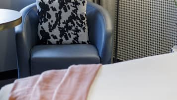 Ein Hotelzimmer mit einem Bett, einem Sessel mit einem gemusterten Kissen, einem Schreibtisch und einer Lampe.