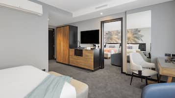 A modern hotel room with a bed, a desk, a chair, a kitchenette, and a TV.