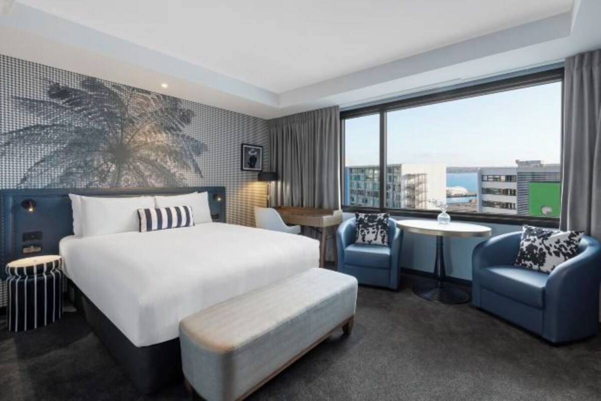 Habitación de hotel moderna con una cama grande, un sofá pequeño, una mesa redonda y vistas a la ciudad.