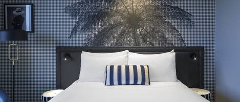 Una cama bien hecha con ropa de cama blanca y un cojín a rayas, un cabecero y una pared con estampado de pied de pito.