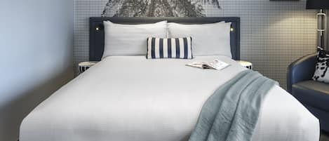 A neatly made bed with white linens, a striped pillow, and a magazine on the bedside table.