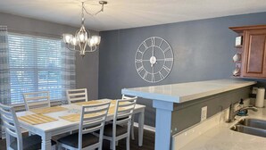 Une cuisine moderne avec un coin repas, agrémentée d’un lustre, d’une horloge murale et d’un évier encastré.