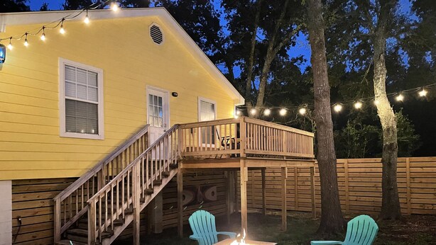 Une maison jaune avec une terrasse en bois, des sièges d’extérieur et des guirlandes lumineuses.