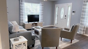 Un salon comprenant un canapé, des fauteuils, une table basse, un téléviseur et une porte ornée de panneaux de verre décoratifs.