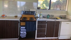A compact kitchen with a stove, sink, and window overlooking a garden.