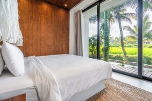 Un dormitorio con una cama grande, paredes de madera y vistas a un paisaje verde exuberante a través de amplios ventanales.