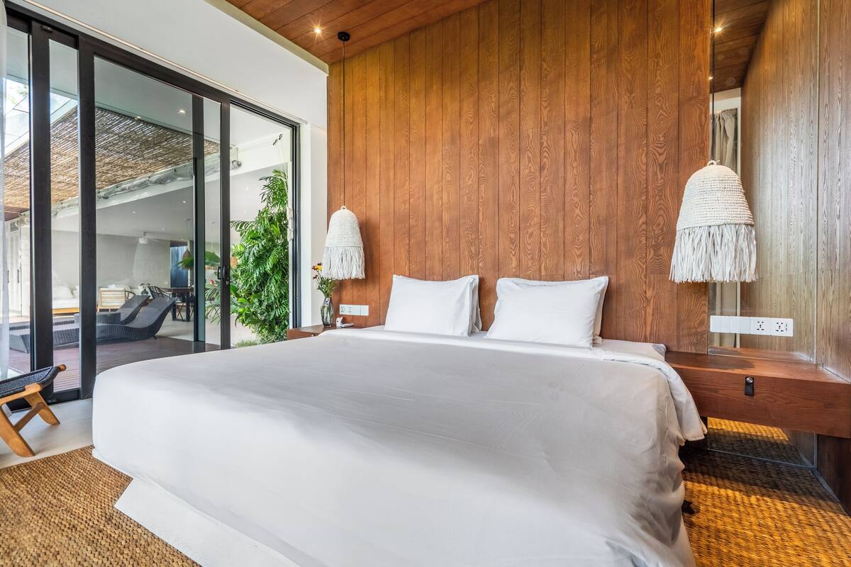 Un dormitorio moderno con una cama grande, paneles de madera y un ventanal corredero que da a un balcón.