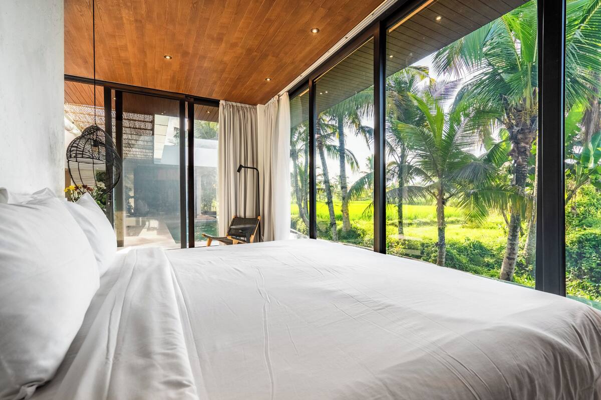 Un dormitorio con una cama grande, vista a palmeras y techo de madera.