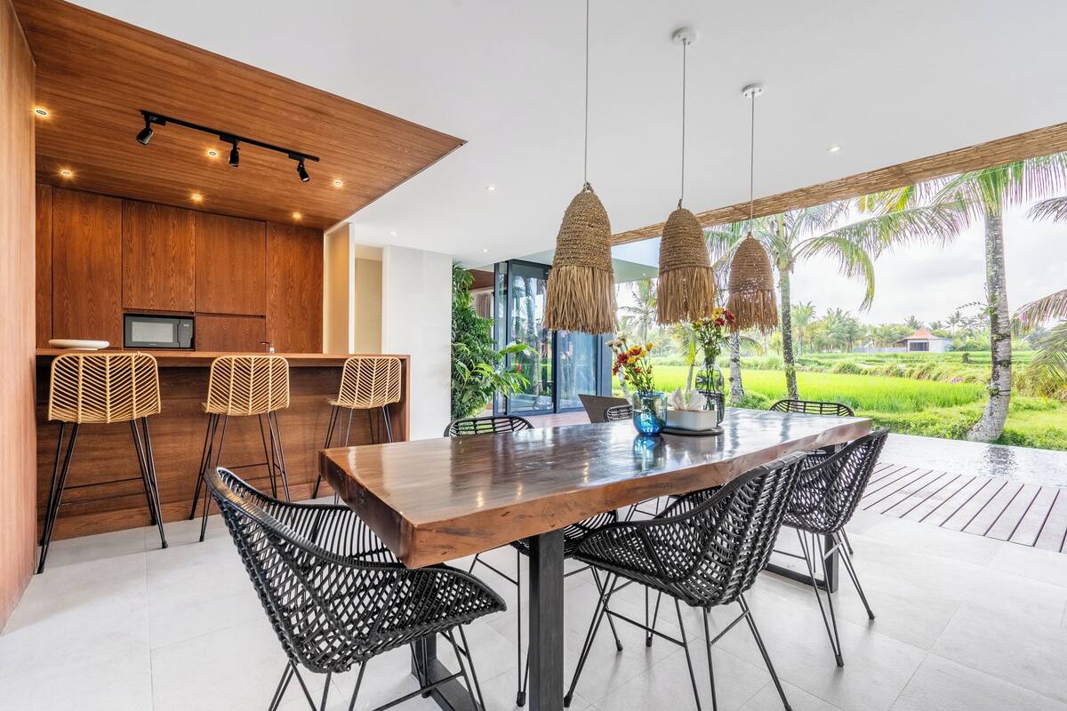 Cocina moderna con armarios de madera, microondas integrado y una zona de bar con sillas de mimbre.