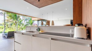 A modern kitchen with a large island, built-in appliances, and a view of lush greenery. - Green Flow Villa 20 (Ubud)