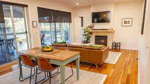 A dining area with a wooden table and chairs, a sofa, and a fireplace. - Fig Tree Guest House (Pokolbin)