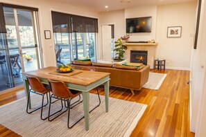 A dining area with a wooden table and chairs, a sofa, and a fireplace. - Fig Tree Guest House (Pokolbin)