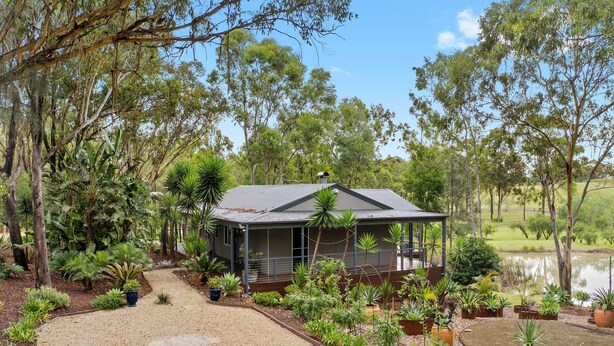 A house with a covered porch, surrounded by a garden with various plants and a pond. - Fig Tree Guest House (Pokolbin)