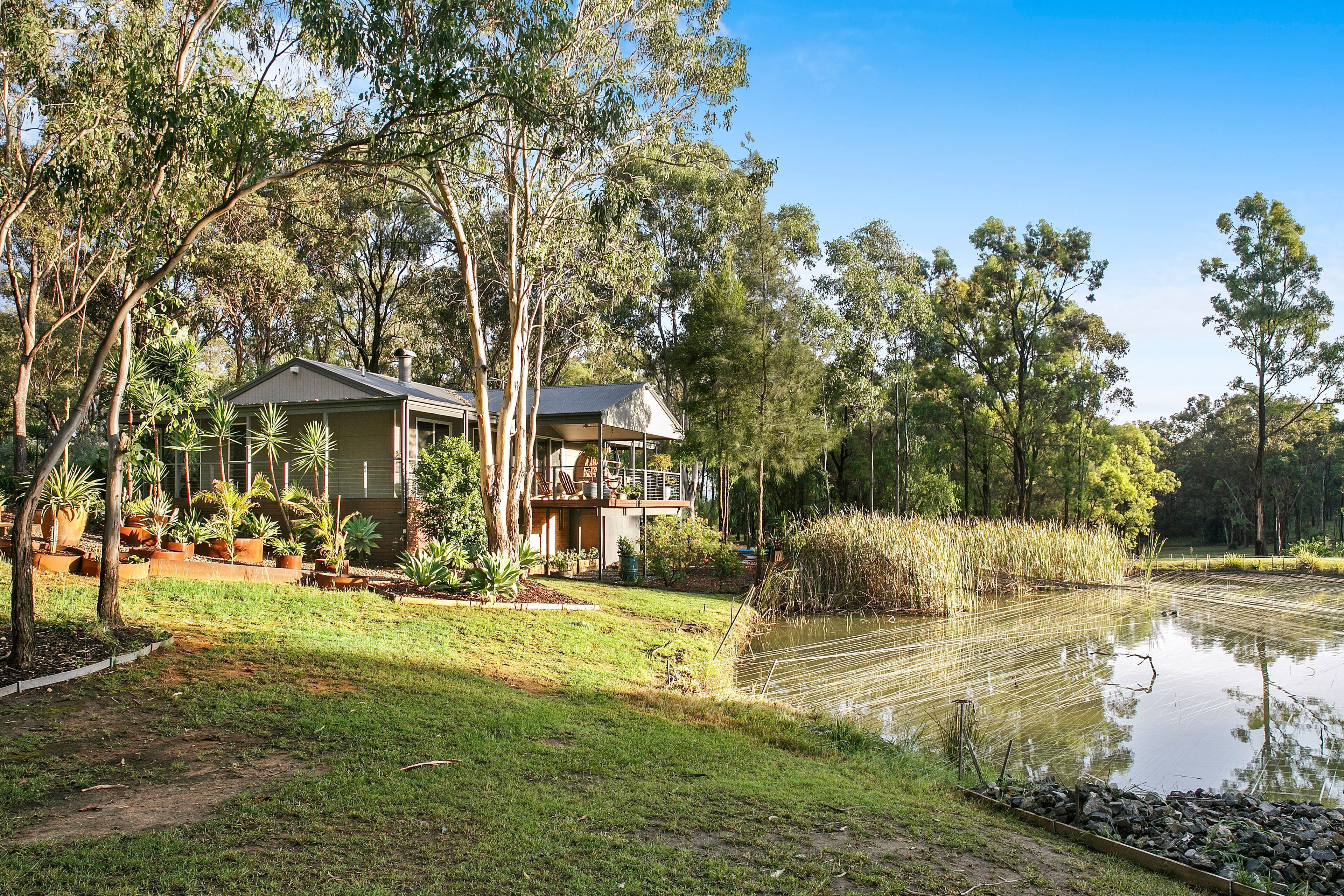 A house with a deck, surrounded by trees and a pond.