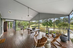 A covered outdoor deck with a table and chairs, overlooking a natural landscape. - Fig Tree Guest House (Pokolbin)