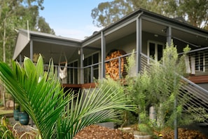 A modern house with a large glass window, surrounded by various plants and trees. - Fig Tree Guest House (Pokolbin)