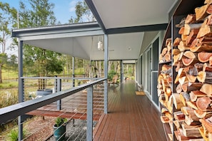 A covered outdoor deck with a wooden floor, metal railings, and a stack of firewood. - Fig Tree Guest House (Pokolbin)