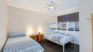 Un dormitorio con dos camas, un ventilador de techo, una mesita de noche y una ventana con vistas.