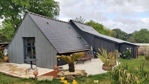 A modern house with a sloped roof, a patio with a table and chairs, and a garden with yellow flowers.