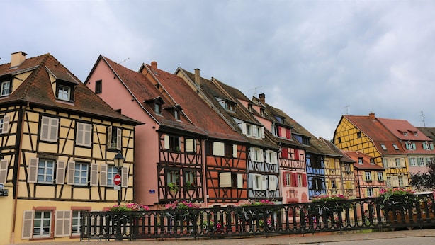Une rangée de maisons traditionnelles à colombages, aux couleurs variées, bordant une rue pavée.