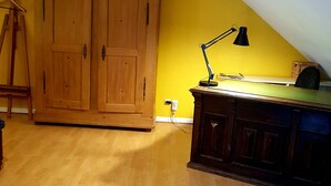 Une pièce avec un plancher en bois, une grande armoire, un bureau avec une lampe et un plafond en pente.