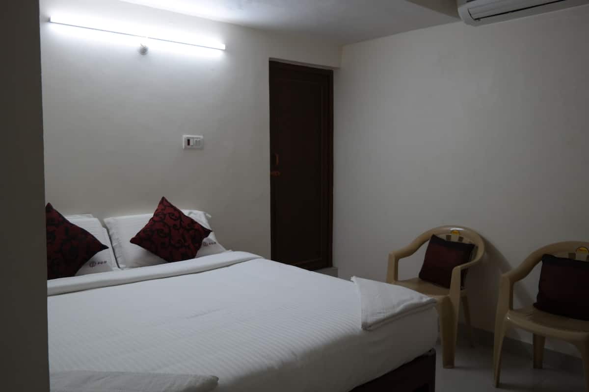 A hotel room with a bed, two chairs, a door, and a wall-mounted air conditioner.