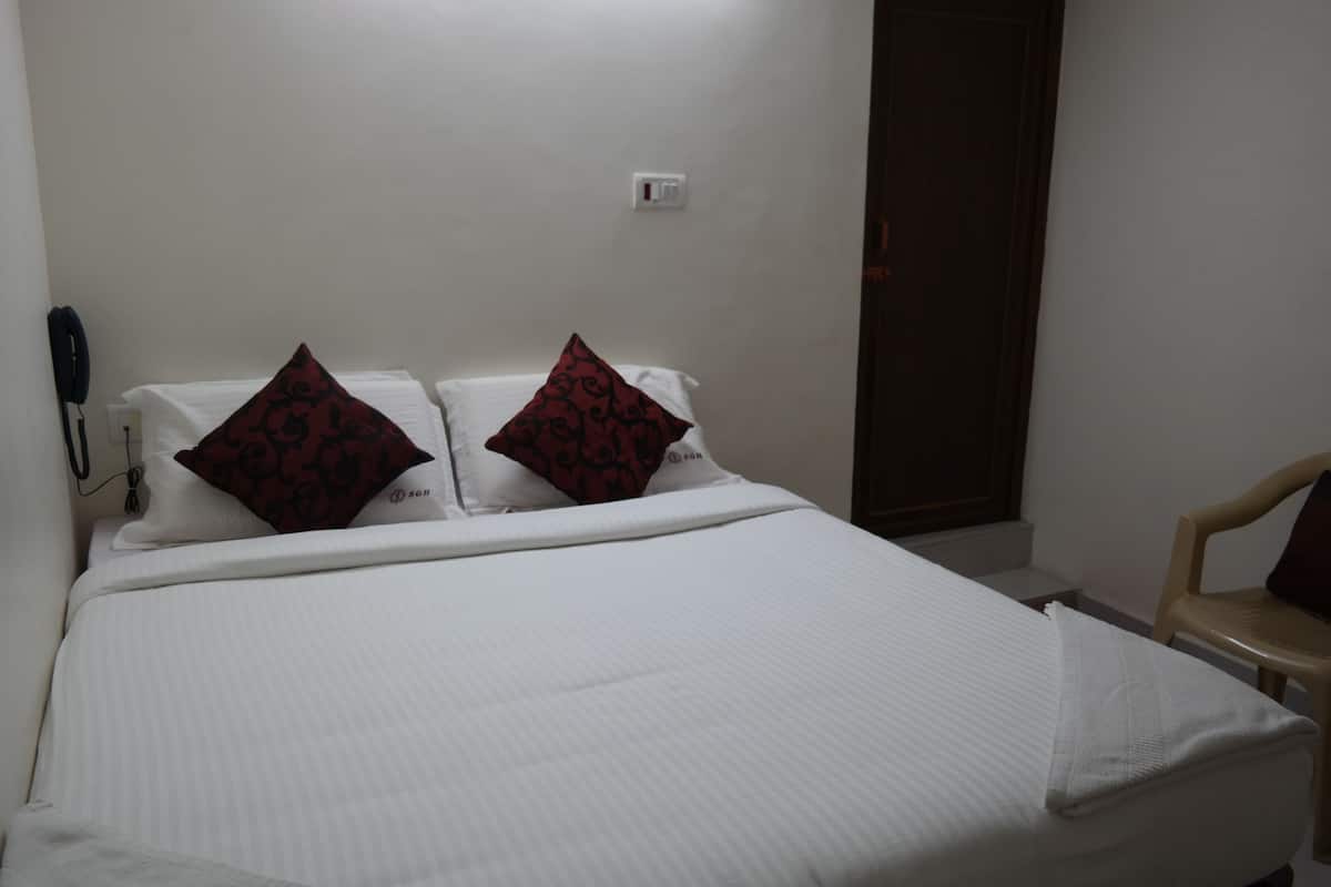 A neatly made bed with white bedding and two decorative pillows, a bedside telephone, and a chair to the right.