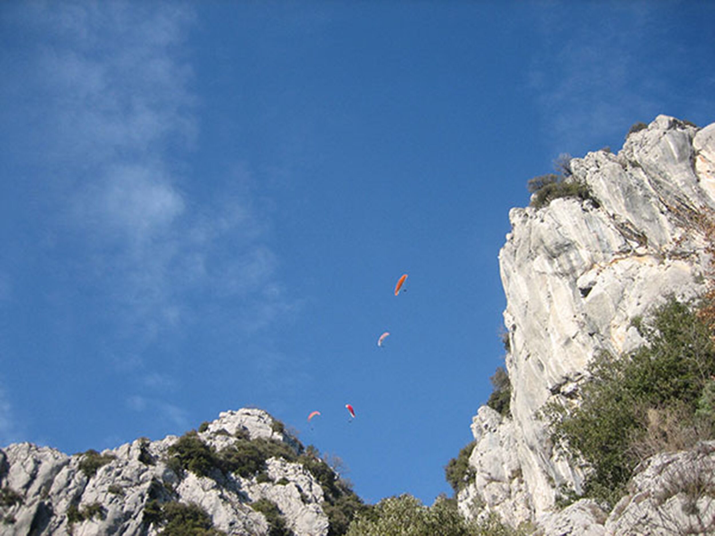 A rocky cliff with a clear sky and several kites flying.