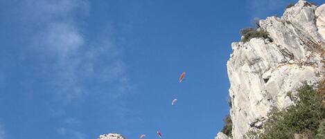 A rocky cliff with a clear sky and several kites flying.