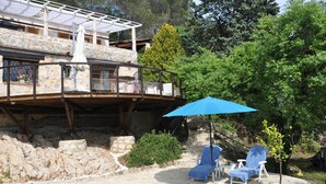 Un bâtiment en pierre doté d’un balcon, d’une piscine et de deux chaises longues sous un parasol bleu.