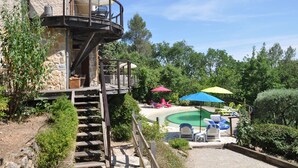 Un espace piscine doté d’une piscine circulaire, de chaises longues et de parasols. Un escalier mène à un balcon d’où l’on peut admirer la vue sur la piscine.