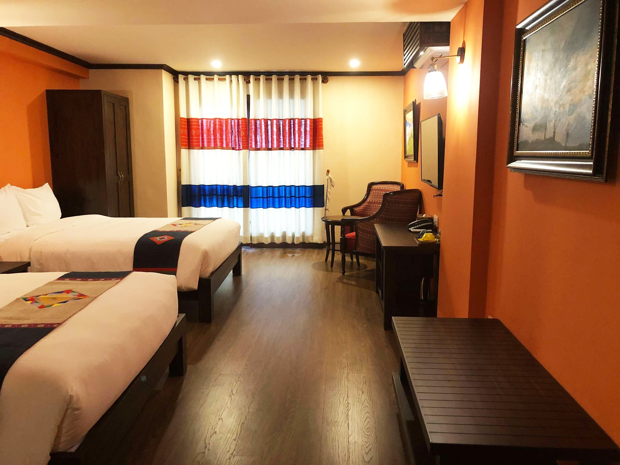 A hotel room with two beds, a desk, a chair, a TV, and a window with curtains.