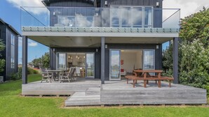 A modern two-story house with a deck, outdoor seating, and a glass balustrade. - Great Matarangi Location Lakeside Gem overlooking the golf course! (Matarangi)