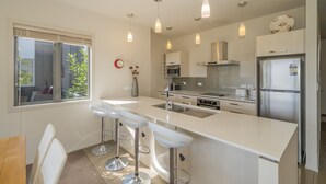 A modern kitchen with a large island, bar stools, stainless steel appliances, and pendant lighting. - Great Matarangi Location Lakeside Gem overlooking the golf course! (Matarangi)