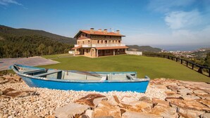 Un edificio de piedra grande con techo plano, rodeado de un césped cuidado y un camino de piedra.
