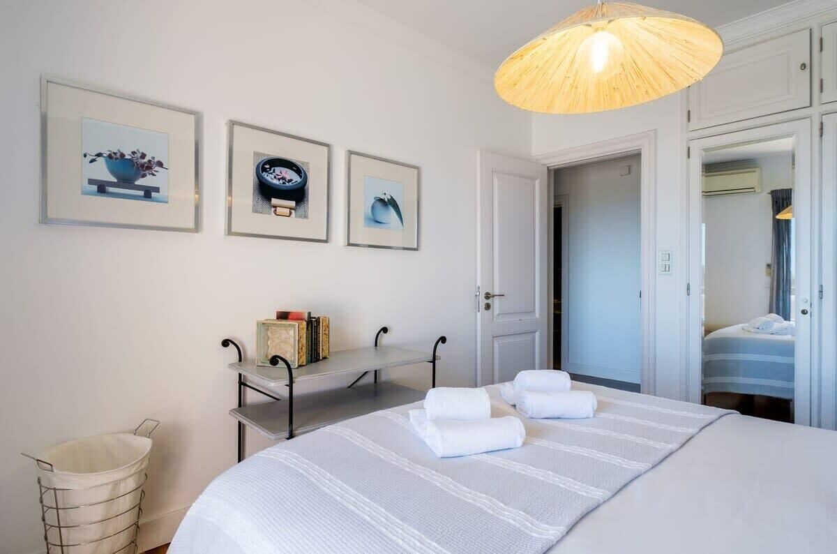 Habitación de hotel con cama, mesita de noche con libros, lámpara y cuadros en la pared.