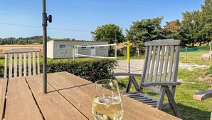 Een houten tafel met een glas witte wijn, twee houten stoelen, een volleybalnet en een klein gebouw op de achtergrond.